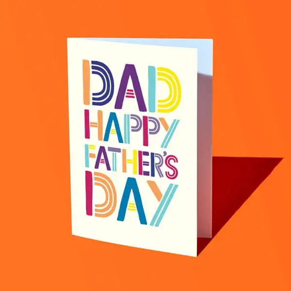 A colourful Fathers Day card with bold patterned lettering reading Dad Happy Father’s Day, displayed against a bright orange background.
